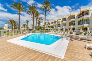 Une piscine avec des chaises longues et des palmiers.