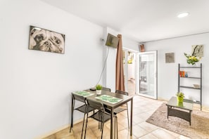 Un coin repas comprenant une table, des chaises, une petite plante en pot et un téléviseur fixé au mur.