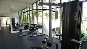 A gym with various exercise machines and a large window providing a view of greenery outside. - By The Sea (George Town)