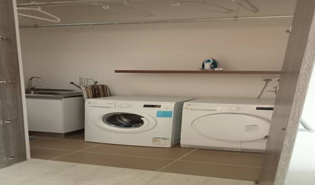 Une buanderie équipée de deux machines à laver, d’un sèche-linge et d’une étagère sur laquelle se trouve une bouilloire.