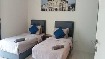Two twin beds with grey headboards and blue pillows, a white wall, and a framed picture of a building.
