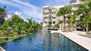 A swimming pool with palm trees and a modern building in the background. - By The Sea (George Town)