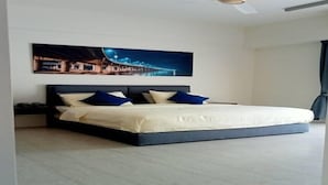A modern bedroom with a large bed, a nightstand, a ceiling fan, and a cityscape painting on the wall. - By The Sea (George Town)