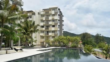 A modern hotel with a pool, palm trees, and a mountainous backdrop.