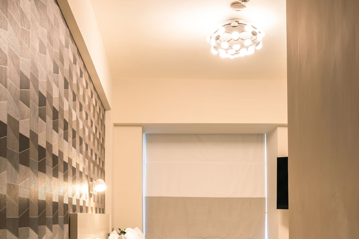A modern bedroom with a geometric-patterned wall, a bed with white linens, and a ceiling light fixture.