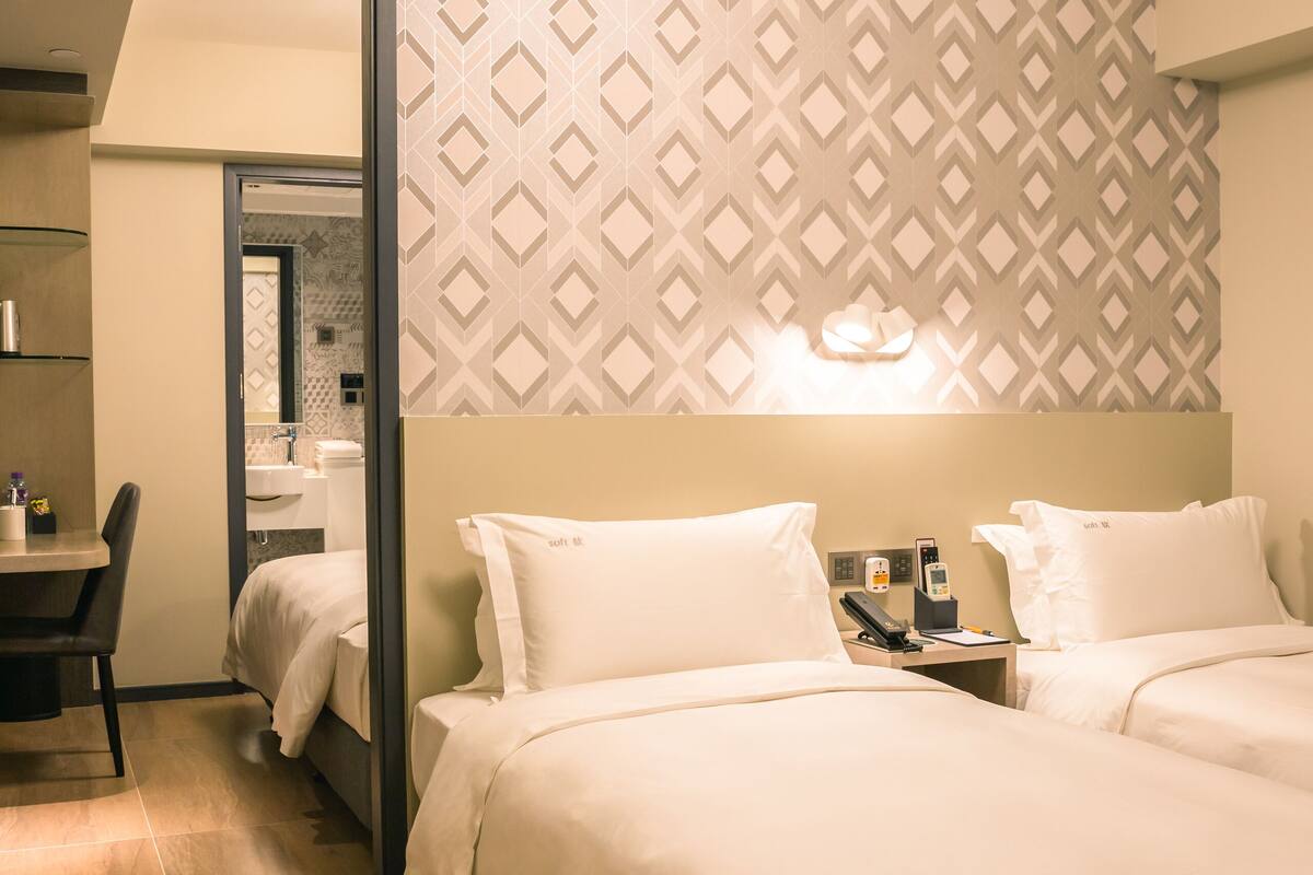 A hotel room with a bed, bedside table, and a mirror.