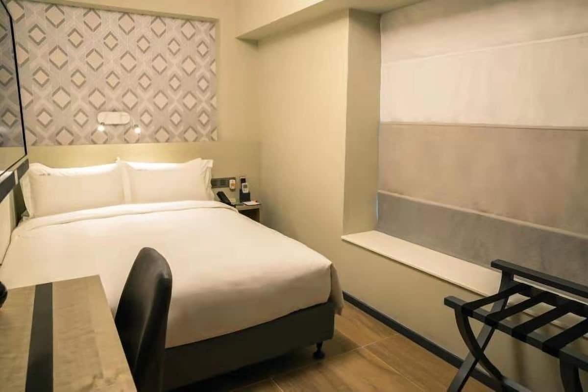 A hotel room with a bed, bedside table, lamp, and a window with a view.