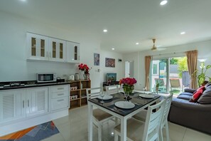 A modern kitchen with white cabinetry, a dining area with a table set for two, and a sofa in the living area.