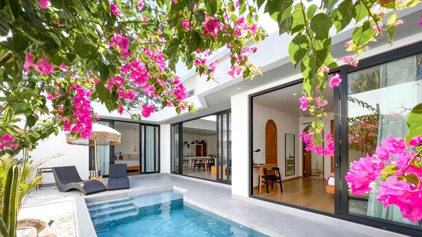 A modern indoor pool area with a glass-enclosed dining area and a seating area with a lounge chair and table. - Villa Cactus Bingin (Pecatu)