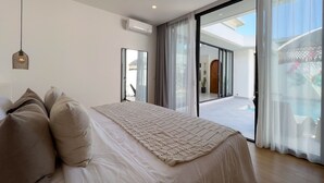 A modern bedroom with a large bed, a ceiling fan, and a view of a pool through a glass door. - Villa Cactus Bingin (Pecatu)