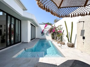 Un espace piscine moderne avec une piscine à l’eau d’un bleu limpide, entourée de murs blancs et dotée d’une entrée en porte vitrée.