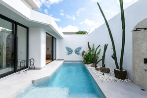 Un espace piscine moderne avec une piscine à l’eau cristalline, des murs blancs et un mobilier minimaliste.