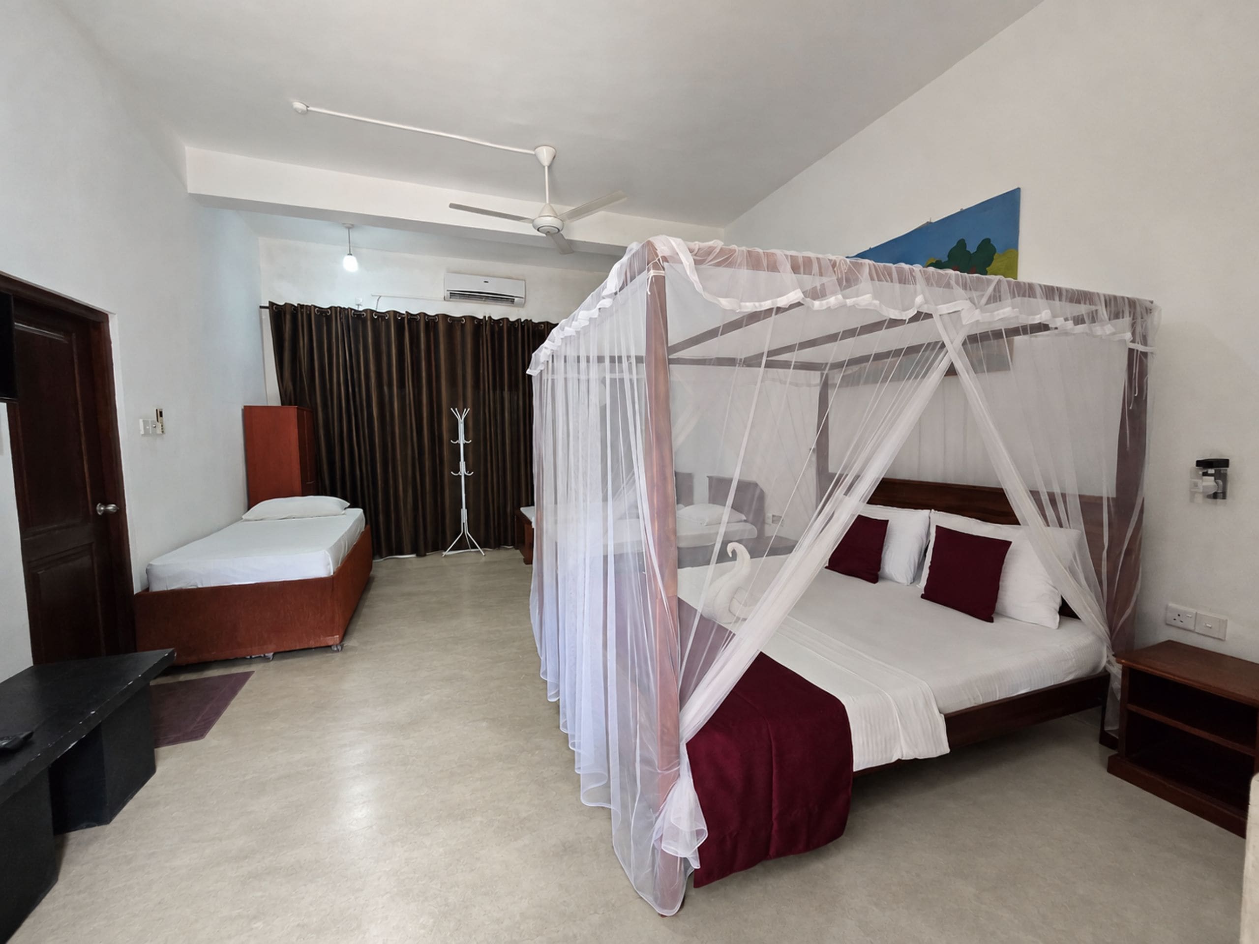 Ein Hotelzimmer mit Himmelbett, Schreibtisch, Stuhl, Garderobe und Deckenventilator.