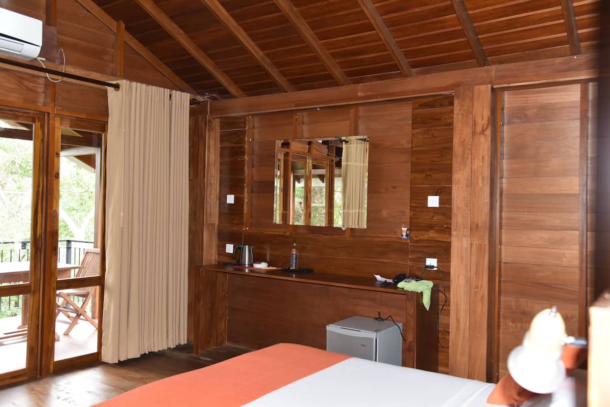A wooden cabin room with a bed, a small desk, a mirror, and a window.