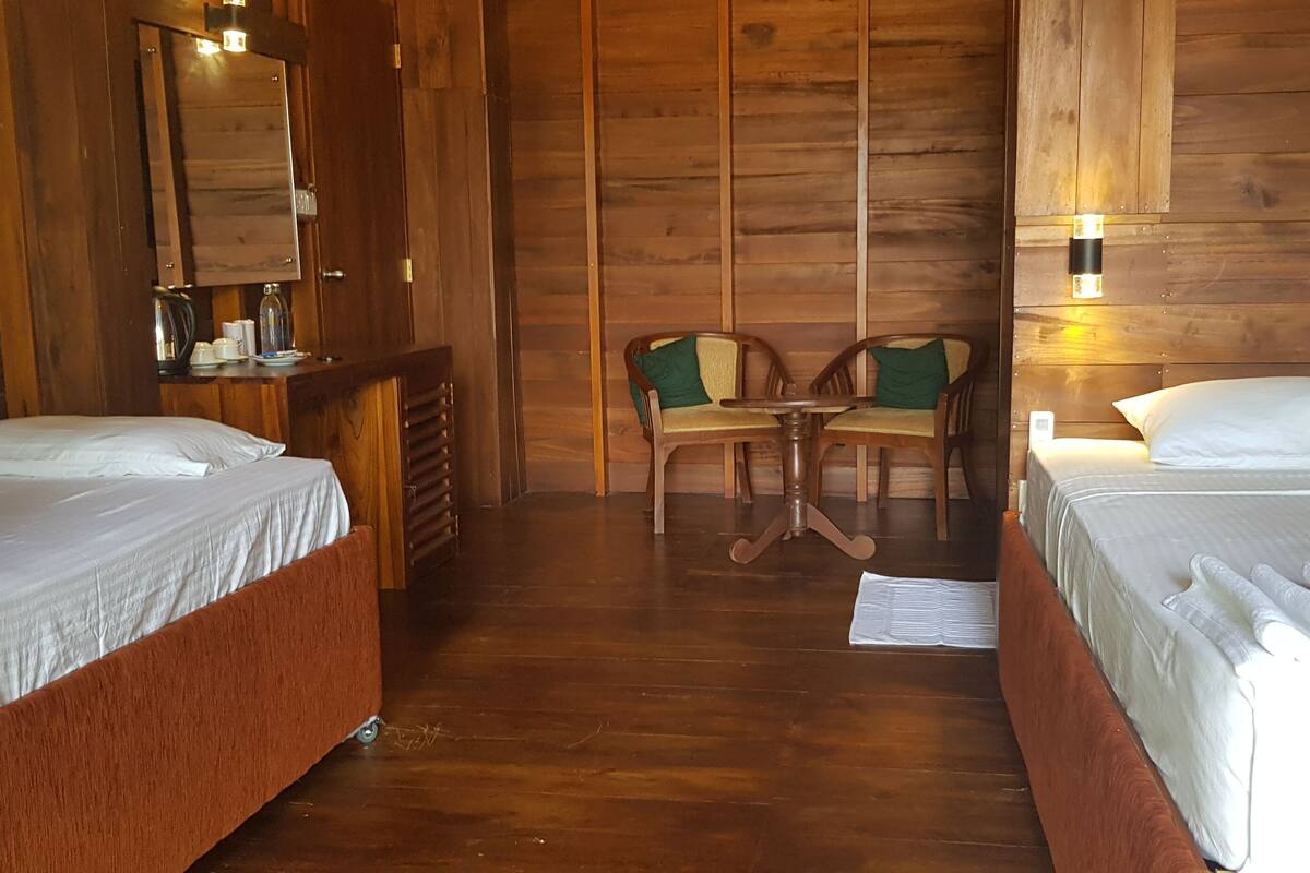 A wooden room with two beds, a small table, chairs, and a mirror.