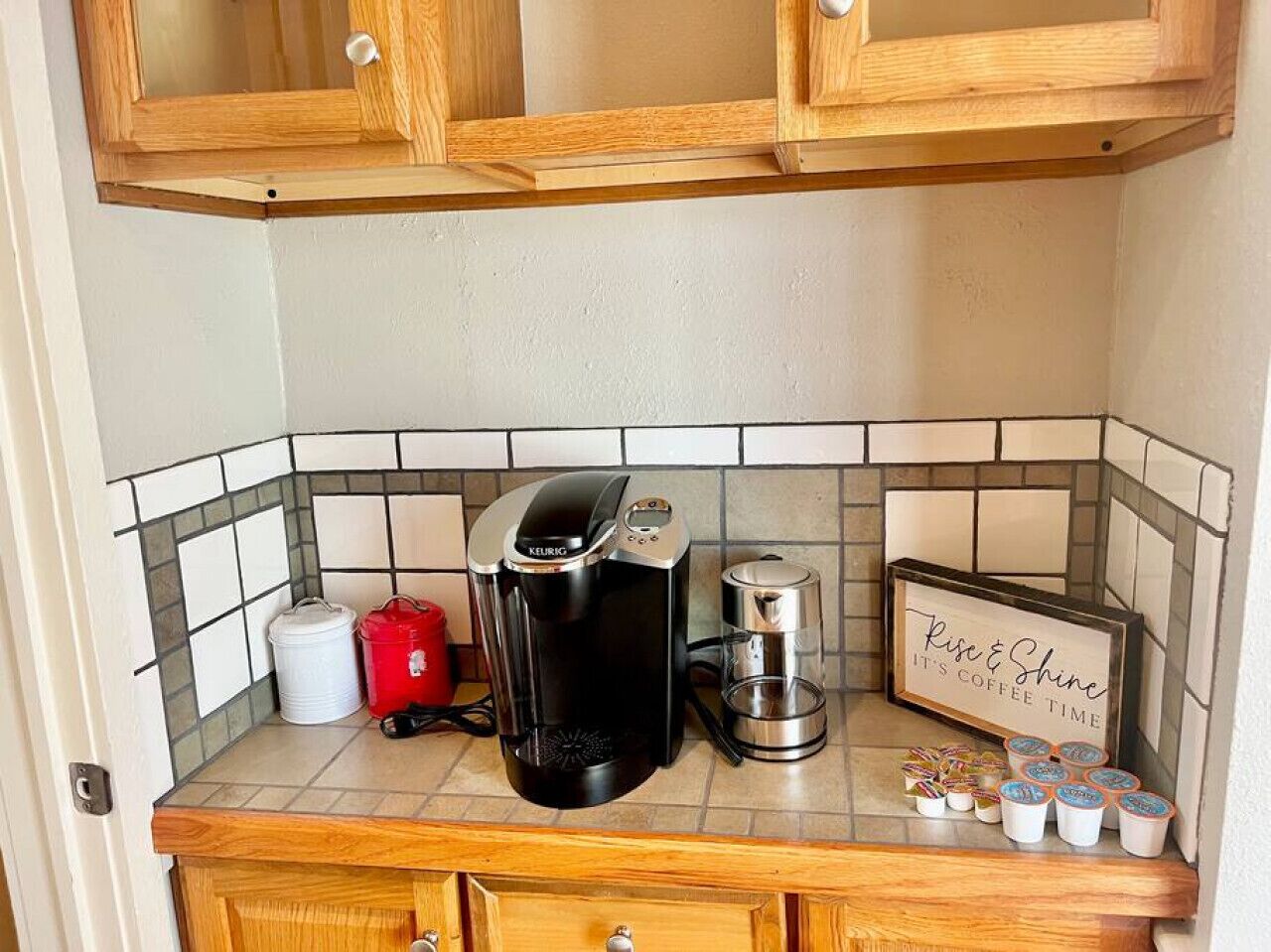A kitchenette with a coffee maker, a kettle, and a coffee-themed sign.
