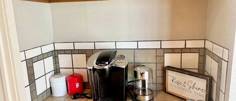 A kitchenette with a coffee maker, a kettle, and a coffee-themed sign.