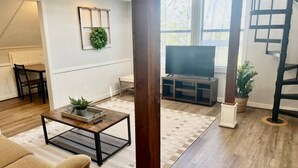 Amplia sala de estar con piso de madera, una mesa de centro, un sofá, un televisor y una escalera.