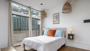 A bedroom with a bed, two bedside lamps, a picture frame, and a large window with curtains.