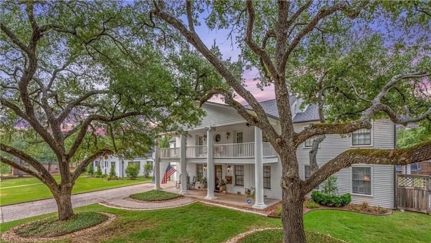 A two-story house with a porch, surrounded by well-maintained lawns and large trees.