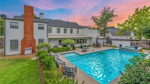 A backyard with a swimming pool, a brick chimney, and a covered patio area.