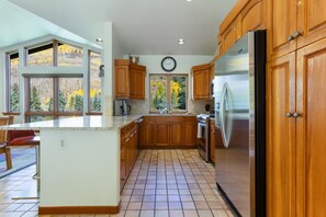 A kitchen with wooden cabinets, a stainless steel refrigerator, and a large window with a view of trees.