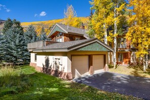 A two-story house with a garage, surrounded by trees and a mountain in the background. - Large East Vail Home - Hot Tub & Steps to Bus Stop (Vail)