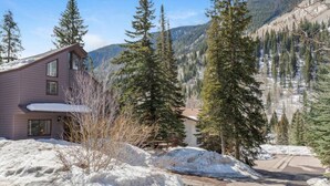 Une maison à deux étages, dont le toit est recouvert de neige, et une allée menant à un point de vue sur la montagne.