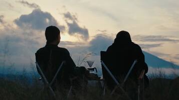 Dos personas sentadas en sillas mirando la puesta de sol con una montaña al fondo.