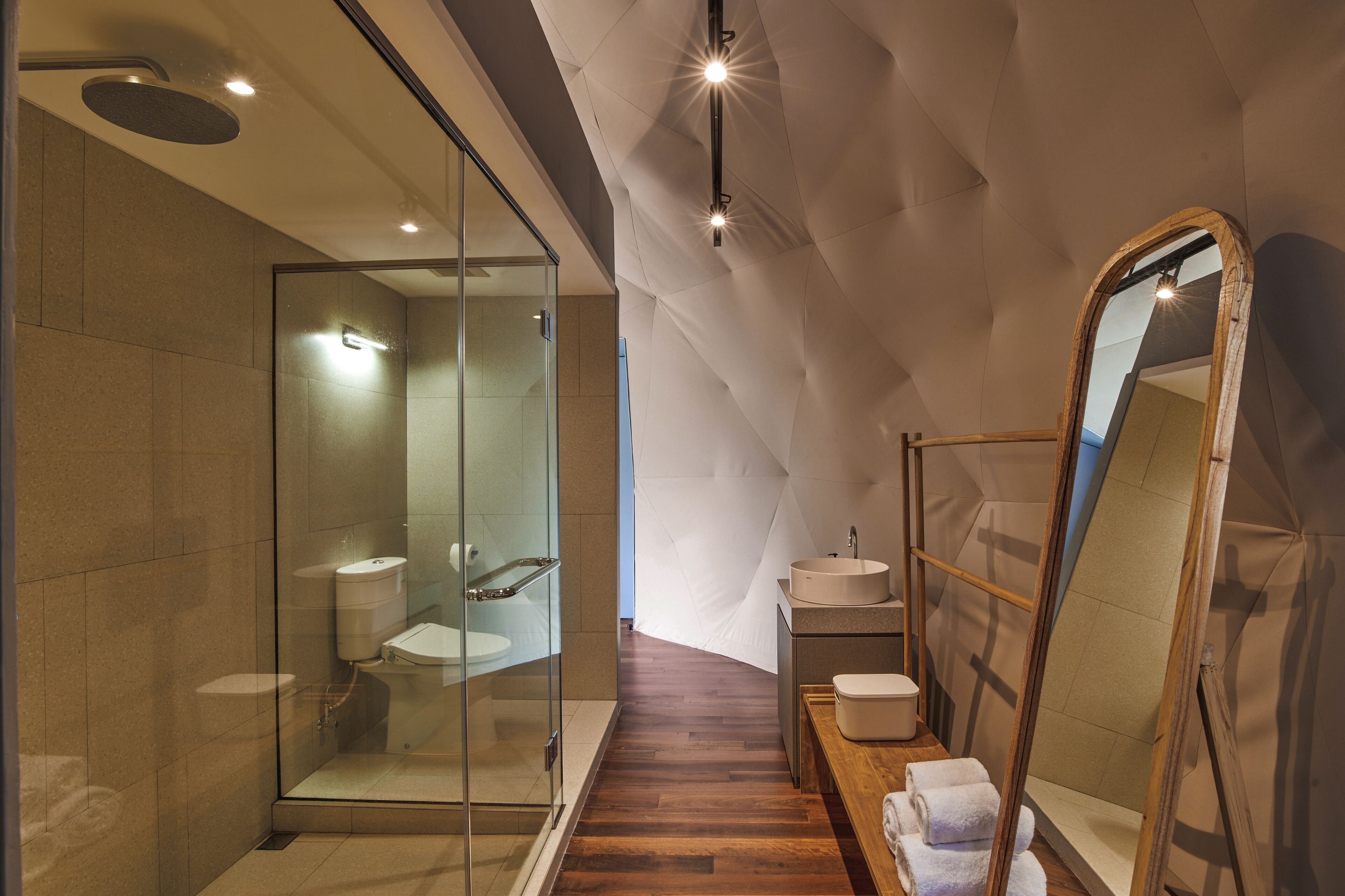 Un baño moderno con ducha de vidrio, banca de madera y un espejo grande.
