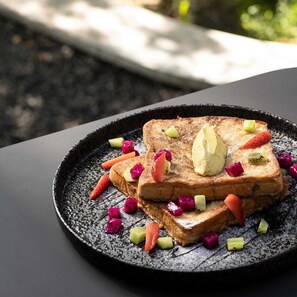 A plate of French toast with fruit and a dollop of butter on a textured black plate. - Lintang Luku Tent Resort Ijen, Banyuwangi (Banyuwangi)