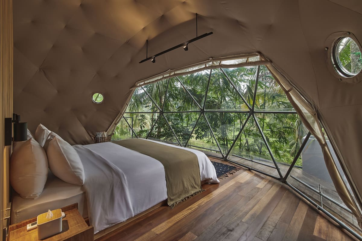Une chambre avec une grande fenêtre, un lit et un plancher en bois.