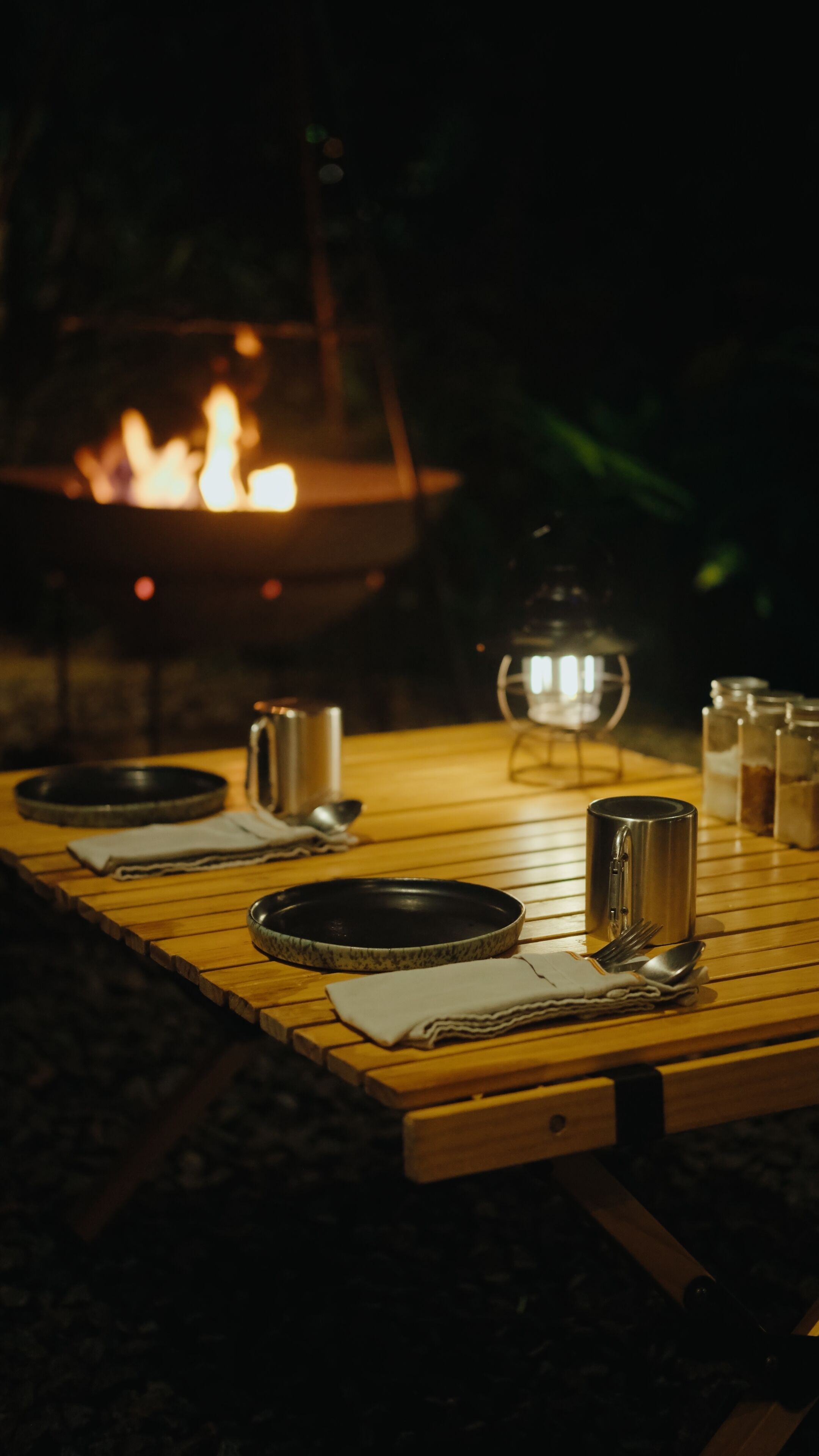 A table set outdoors at night with a fire in the background.