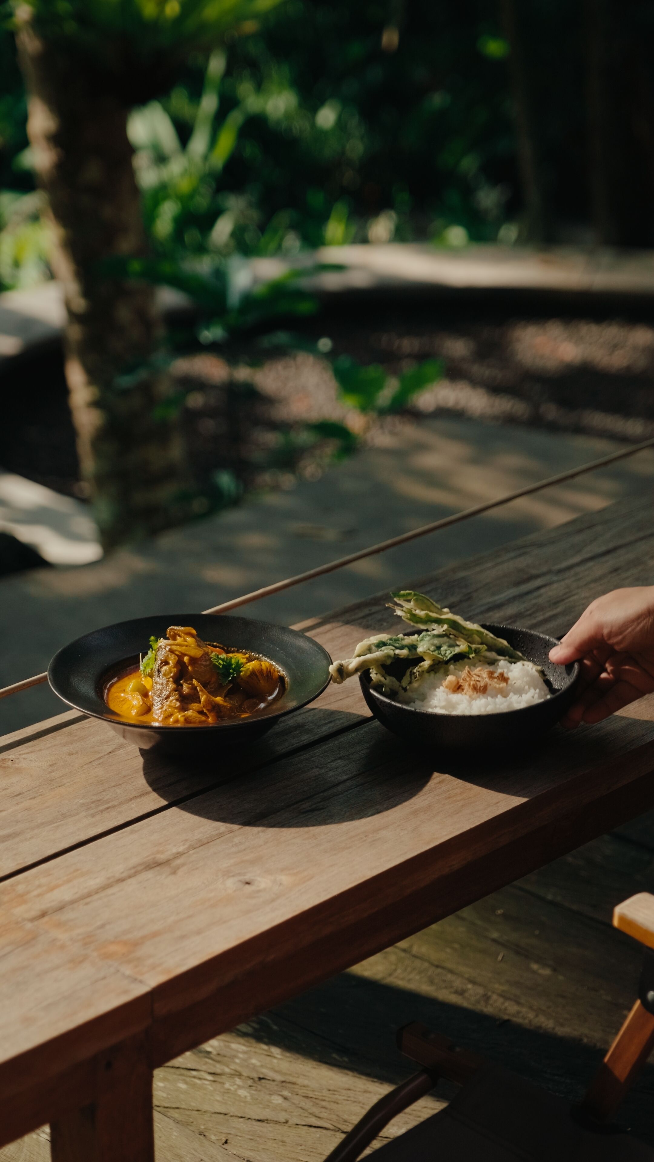 Une table en bois sur laquelle se trouvent deux bols de nourriture : l’un contient un plat de curry, l’autre du riz et des légumes.