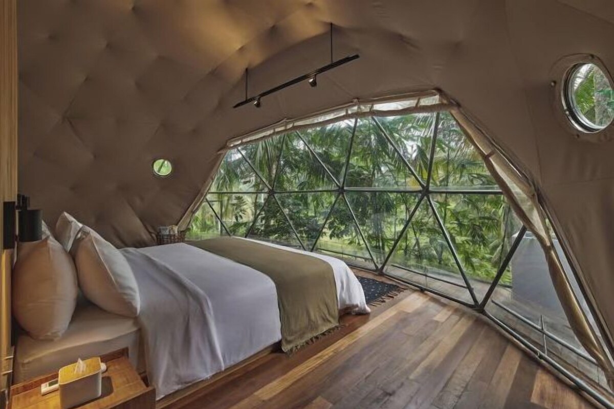Une chambre avec une grande fenêtre, un plancher en bois et un lit avec des oreillers.