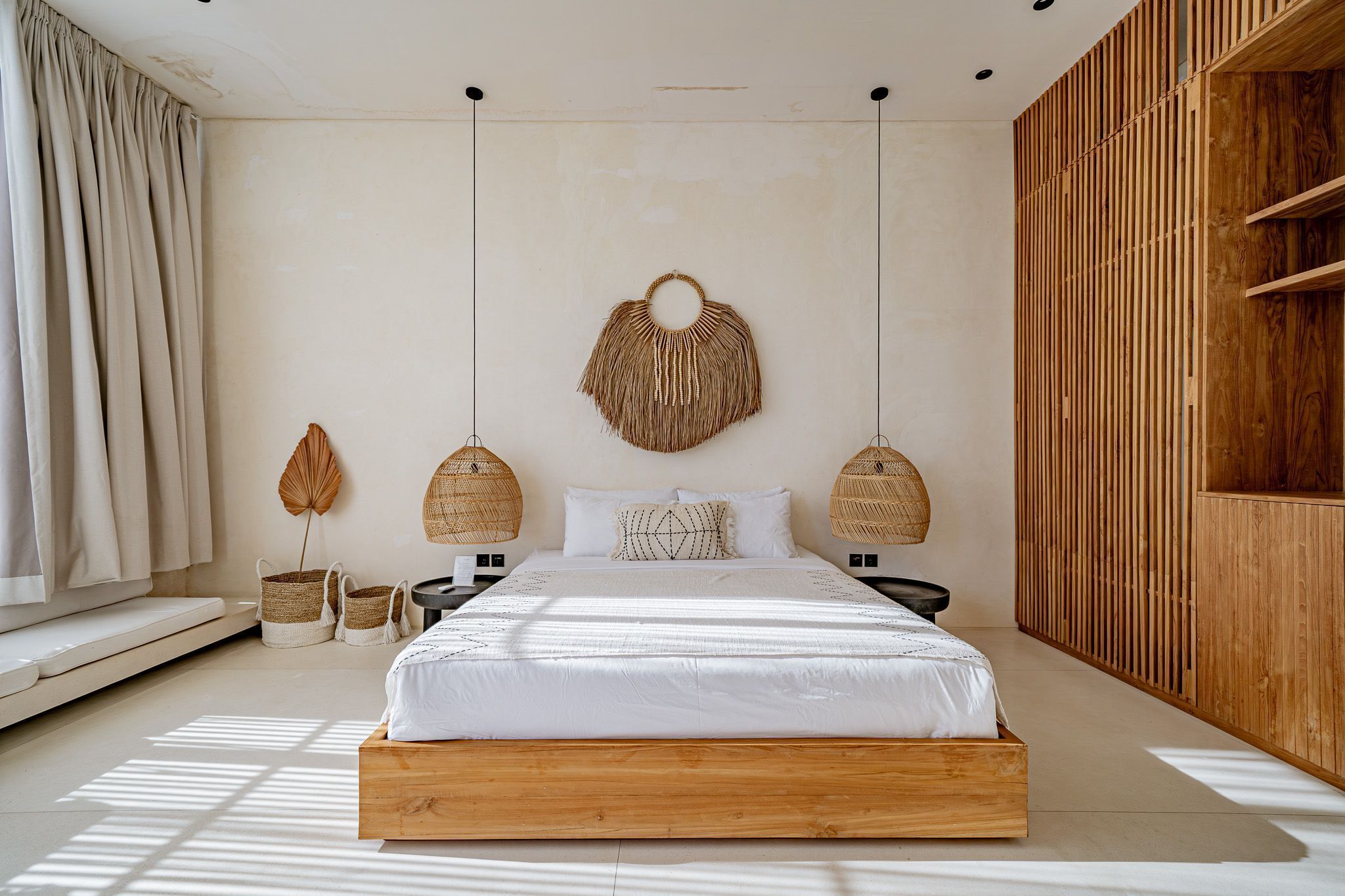 Une chambre à coucher au style minimaliste, avec un cadre de lit en bois, une grande tapisserie murale tissée et deux appliques murales en osier.