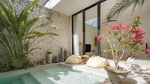 A pool area with a stone wall, large potted plants, and a seating area with cushions. - Casa Noema (Kerobokan)