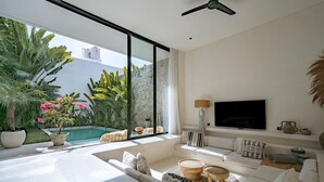 Ein modernes Wohnzimmer mit großem Fenster, Flachbildfernseher und Blick auf einen Pool.