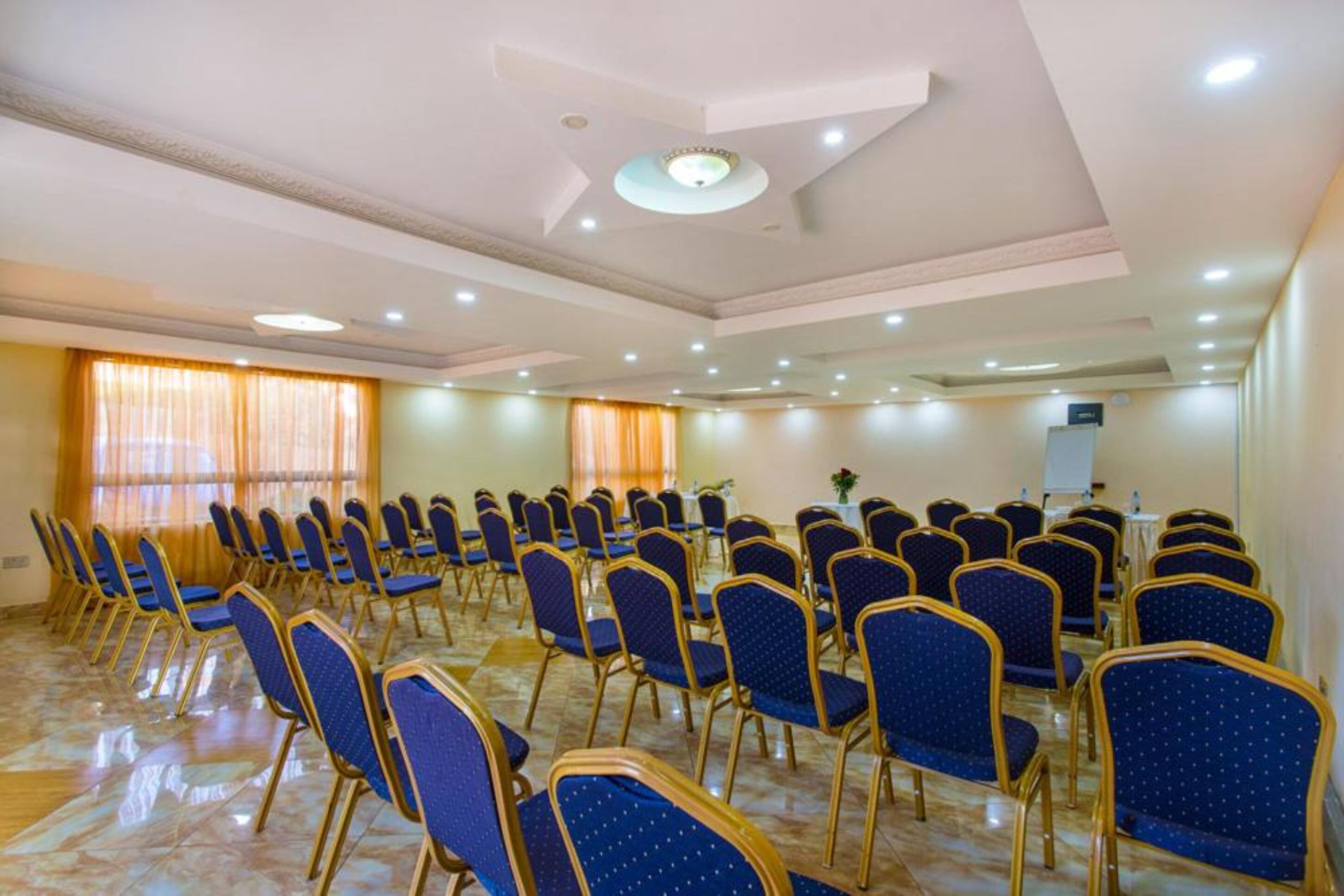 Un salón de conferencias con filas de sillas azules, un atril y un amplio ventanal con cortinas.