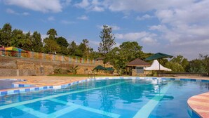 Una piscina con un borde empinado de baldosas, un pequeño pabellón y un área cercada con estructuras coloridas.