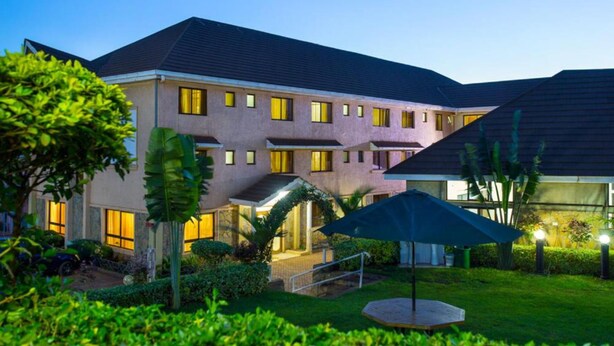 Un hotel de varios pisos con techo plano, múltiples ventanas y un jardín cuidado con un gran paraguas.