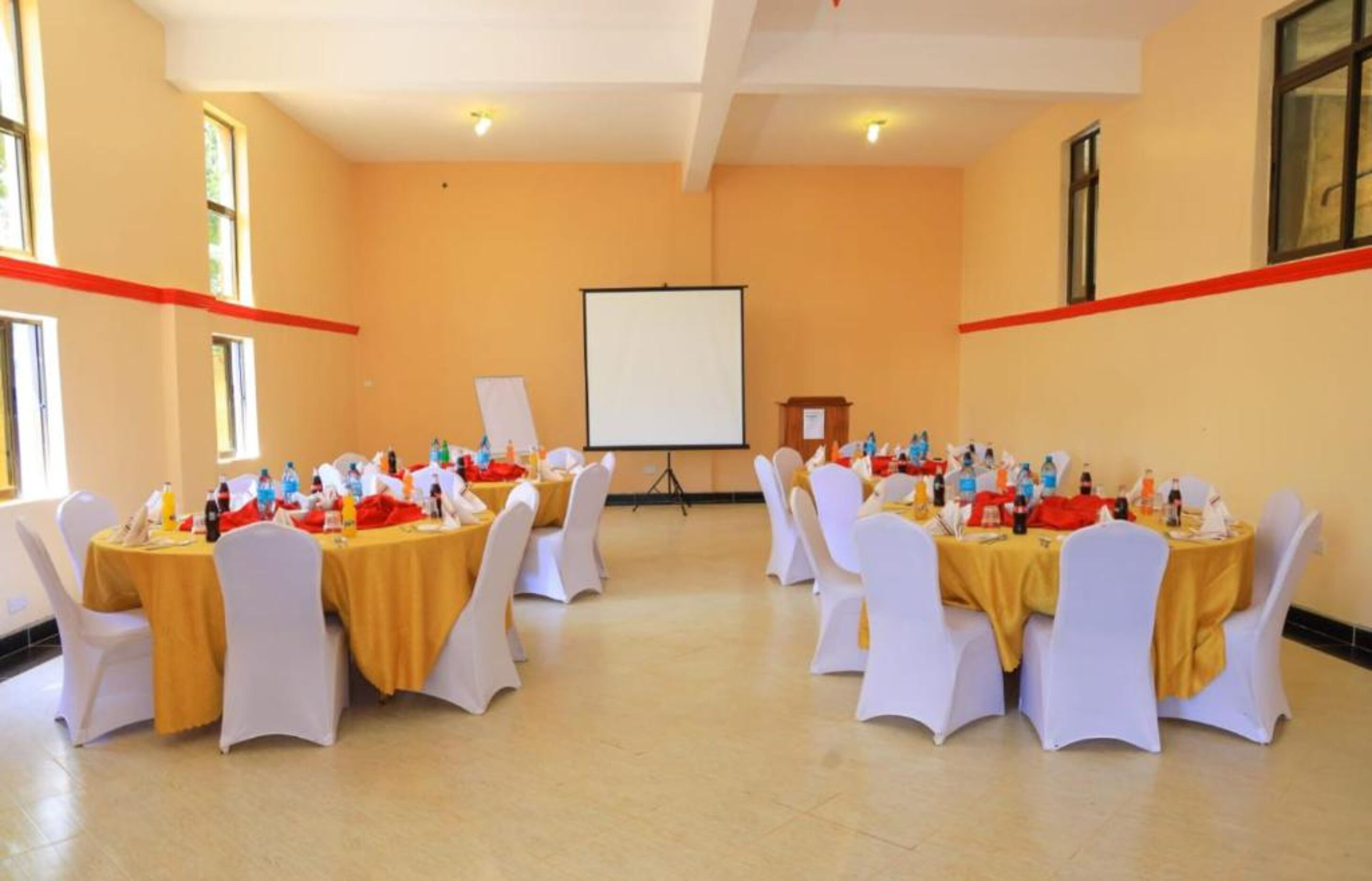 A conference room with tables set for a meeting, white chairs, a projector screen, and a podium.