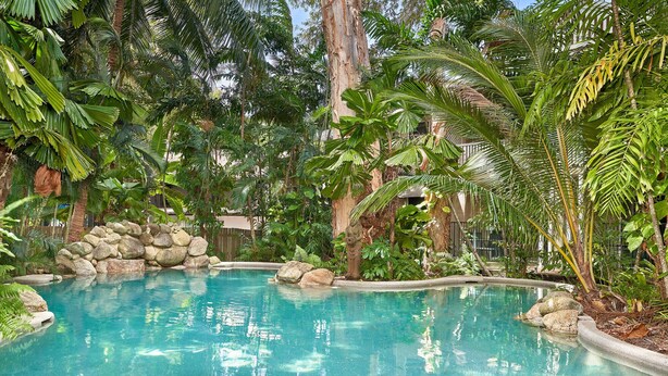 Ein klares, blaues Schwimmbecken, umgeben von tropischer Vegetation und Felsen.