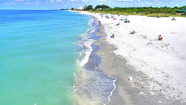 A beach with clear turquoise water, sandy shore, and people relaxing.