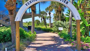 A sign for Venice Fishing Pier with a pathway leading through a tropical garden.