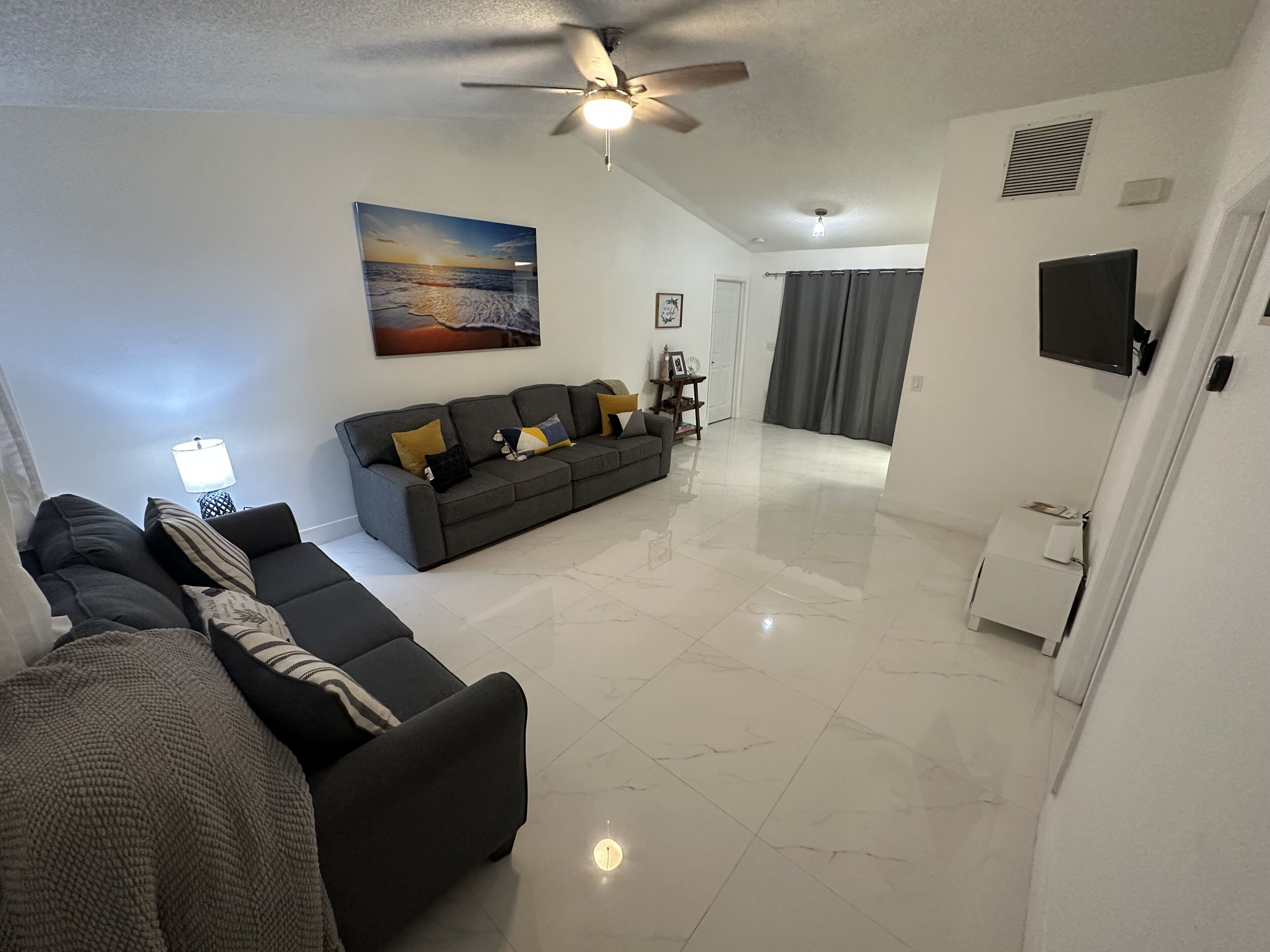A living room with a sofa, a ceiling fan, a painting, and a television.