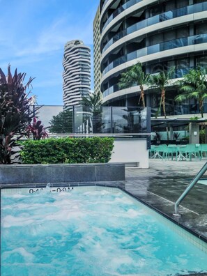 A modern hotel with a rooftop pool, surrounded by lush greenery and palm trees.
