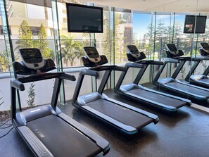 A gym with treadmills, exercise bikes, and a large window with a view of buildings and trees.