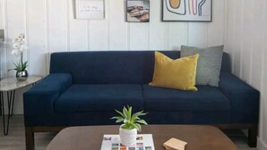 Un salon avec un canapé bleu foncé, une table basse ornée d’une plante et divers tableaux encadrés accrochés au mur.