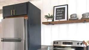 Une cuisine moderne dotée d’un réfrigérateur en acier inoxydable, d’un four encastré et d’une étagère en bois au-dessus de la cuisinière.